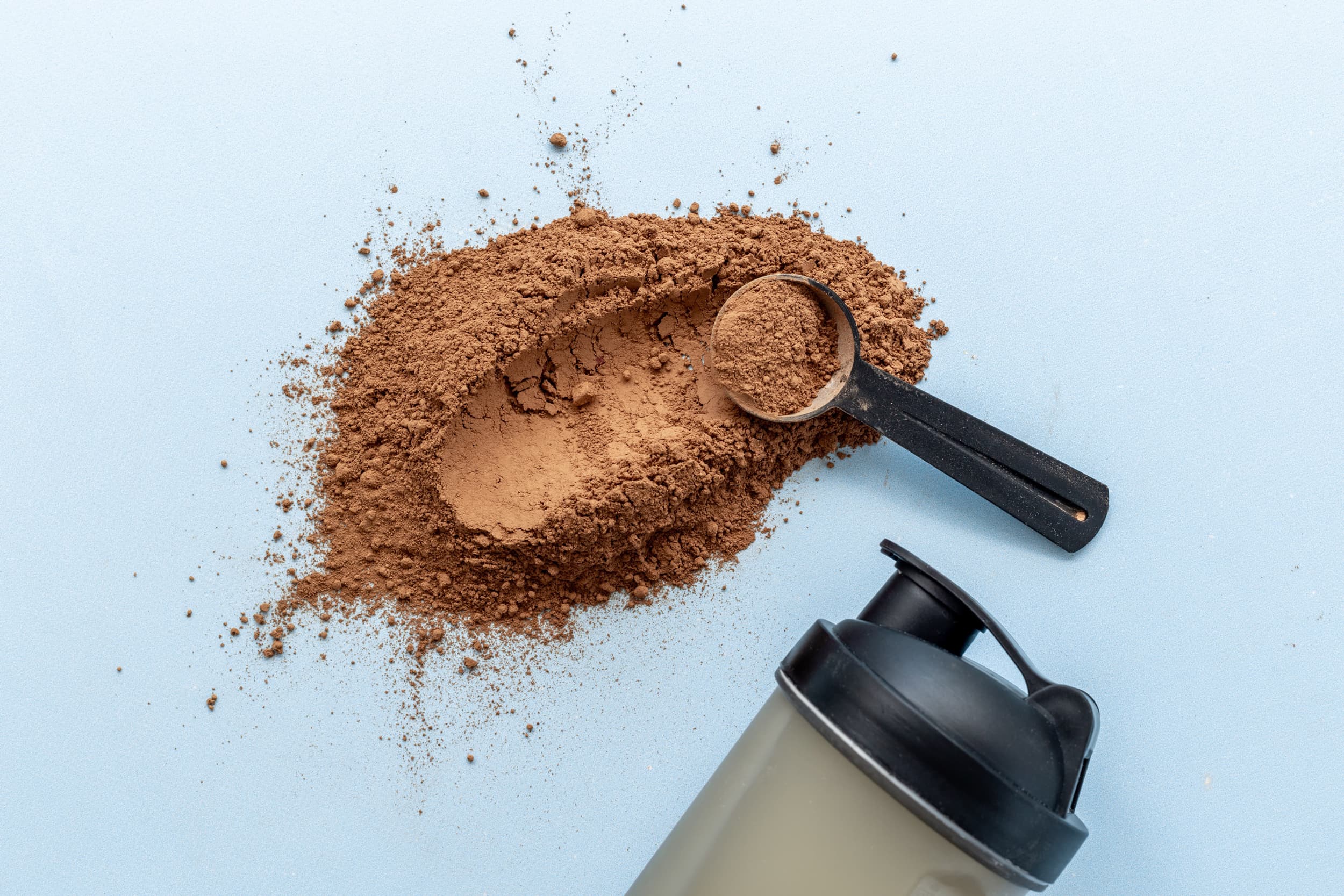 Proteine naturali in polvere e shaker Protéalpes su sfondo blu, senza edulcoranti né additivi, per l'alimentazione sportiva.