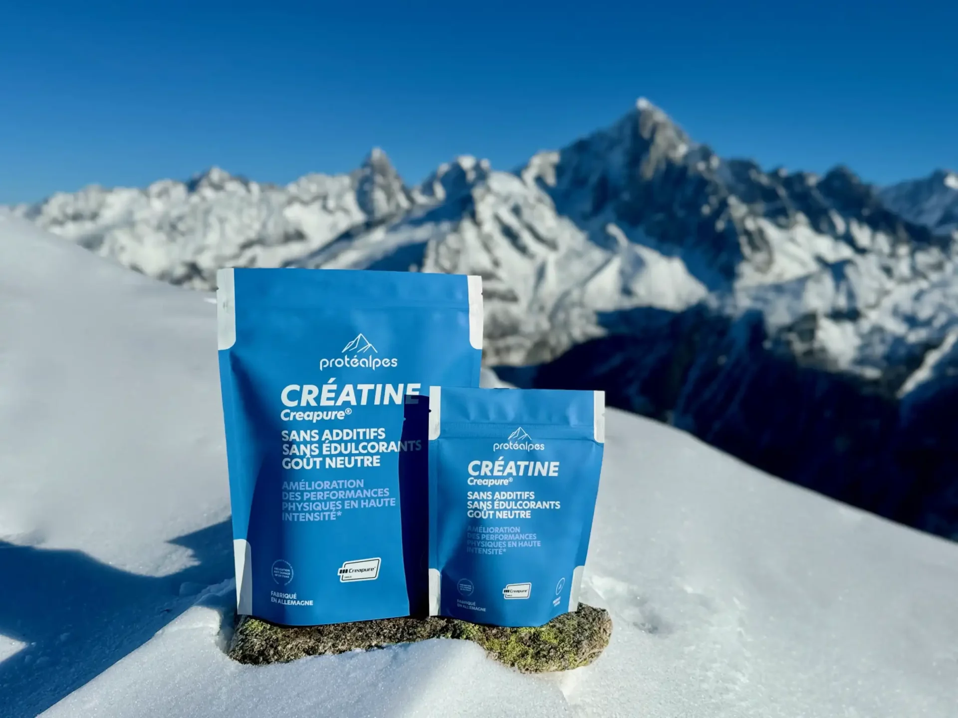 Protéalpes creatine sachets with no additives or sweeteners, sitting on the snow with a view of the mountains in the background.