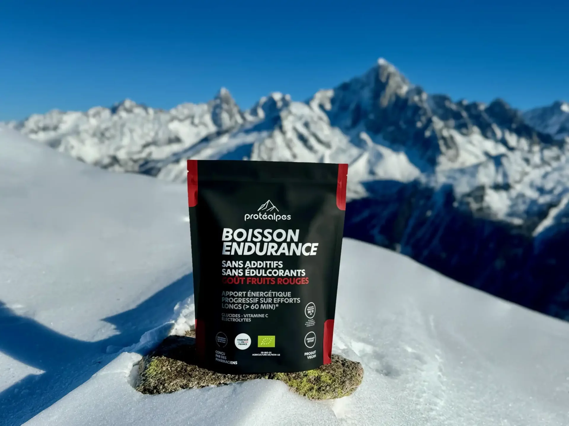 Boisson Protéalpes sans édulcorants ni additifs, goût fruits rouges, posée sur la neige avec des montagnes en arrière-plan.