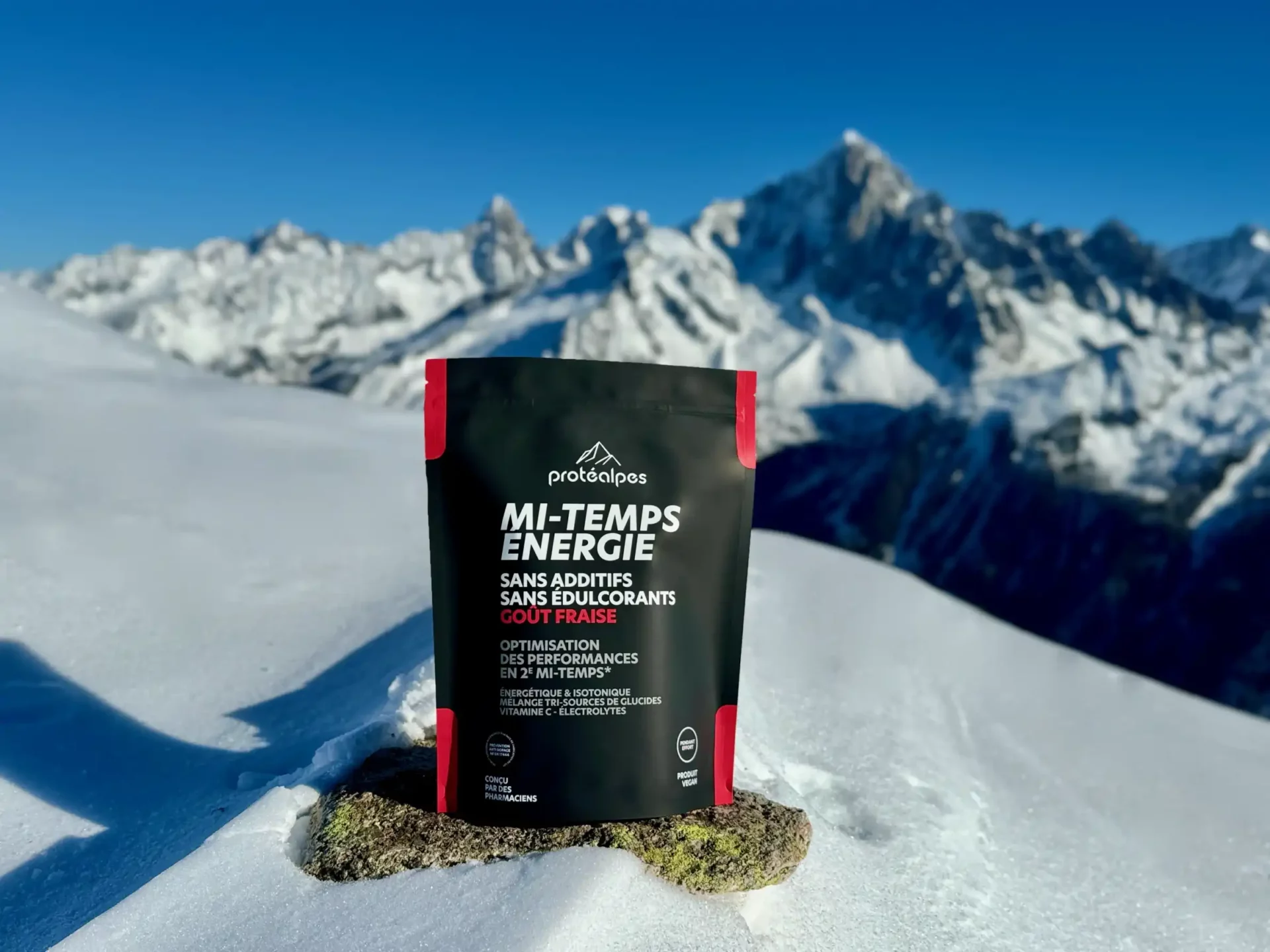 Mi-Temps Énergie by Protéalpes, with no additives or sweeteners, placed on snow in front of snow-capped mountains.