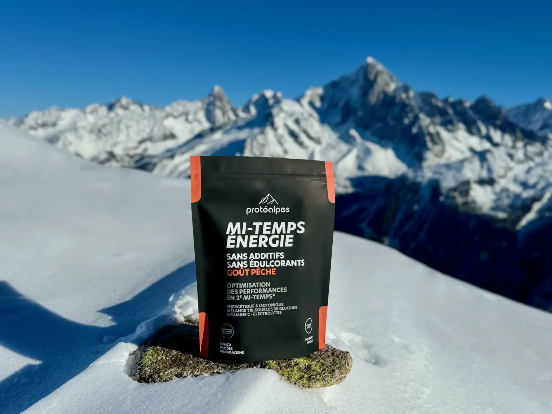 Confezione di Protéalpes Mi-Temps Energy senza additivi né dolcificanti, ambientata sulla neve con le montagne sullo sfondo.