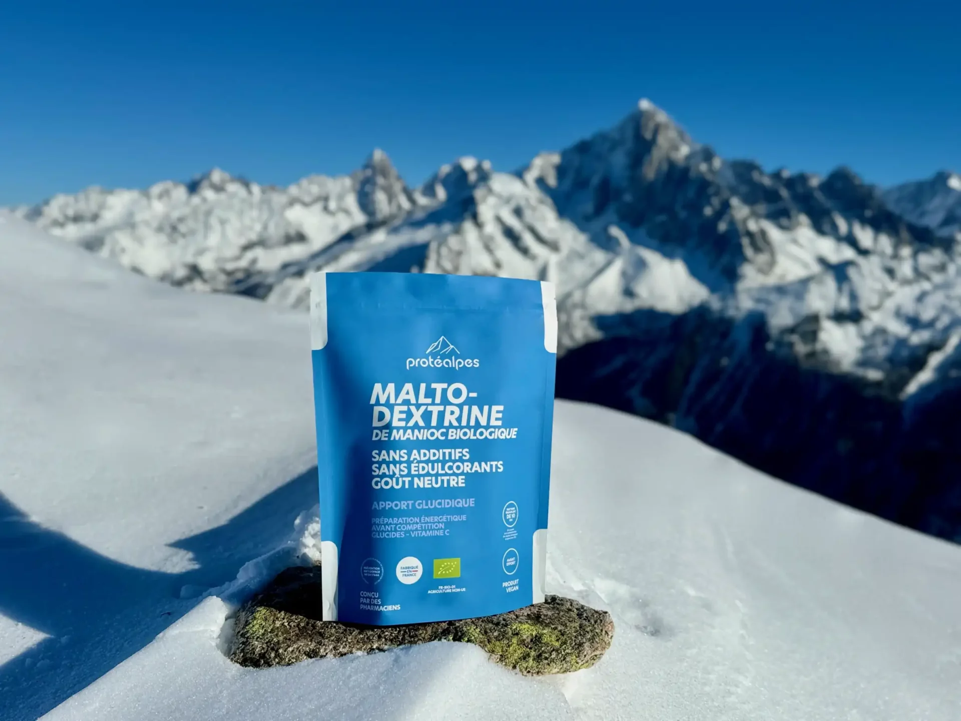 Beutel Maltodextrin Protealpes auf Schnee, vor schneebedeckten Bergen, betont Sporternährung ohne Süßstoffe und Zusatzstoffe.