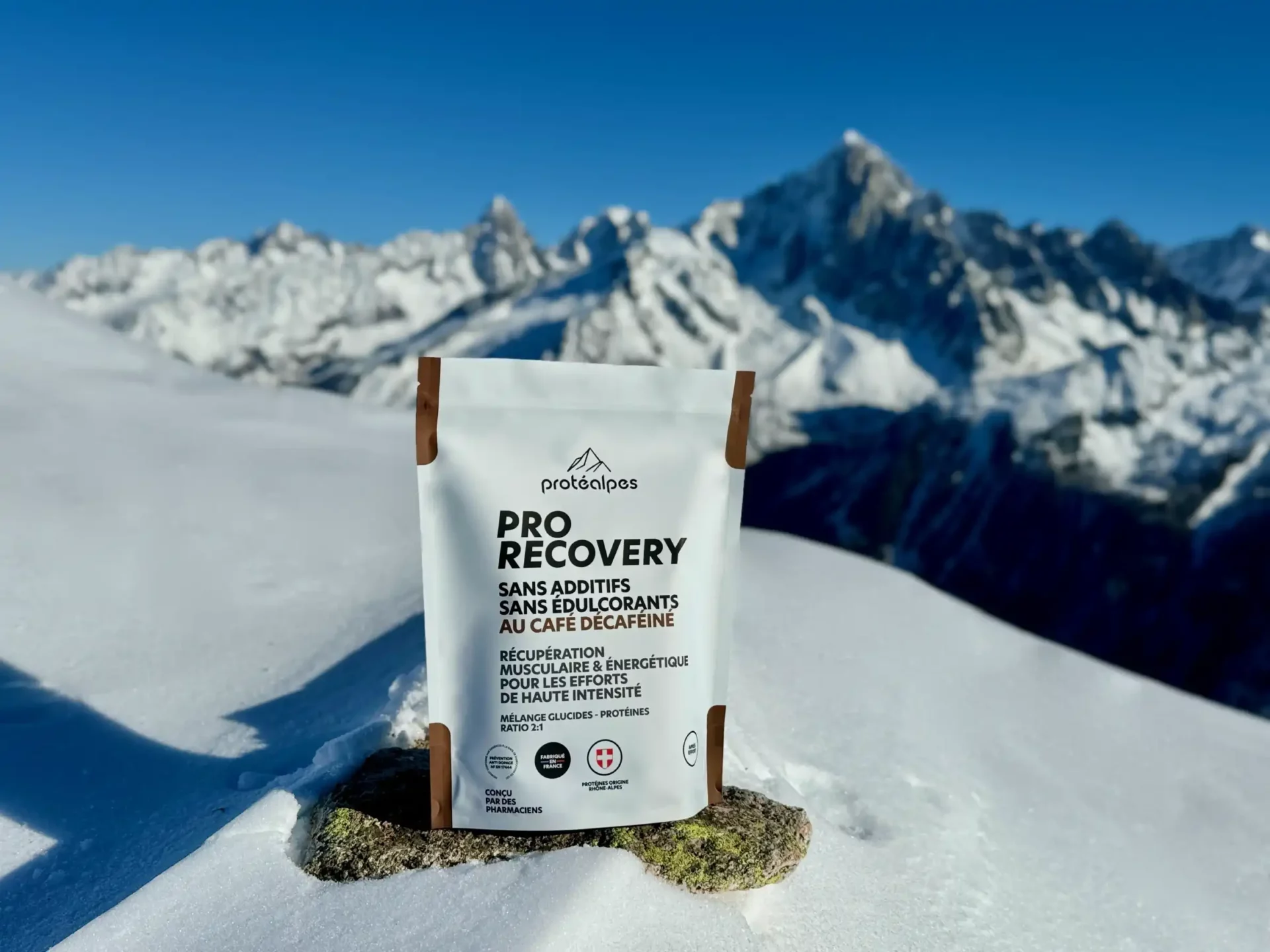 Produit Protéalpes Pro Recovery naturel, sans additifs ni édulcorants, posé dans un paysage enneigé alpin, ciel bleu.