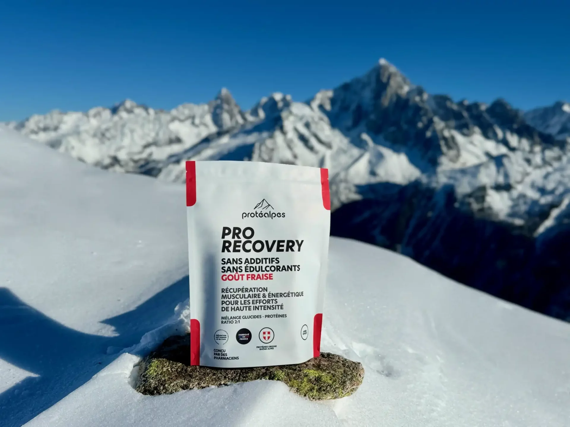 Produkt ProRecovery Proteinalpes vor einem verschneiten alpinen Hintergrund, Sporternährung ohne Zusatzstoffe oder Süßstoffe, Erdbeergeschmack.
