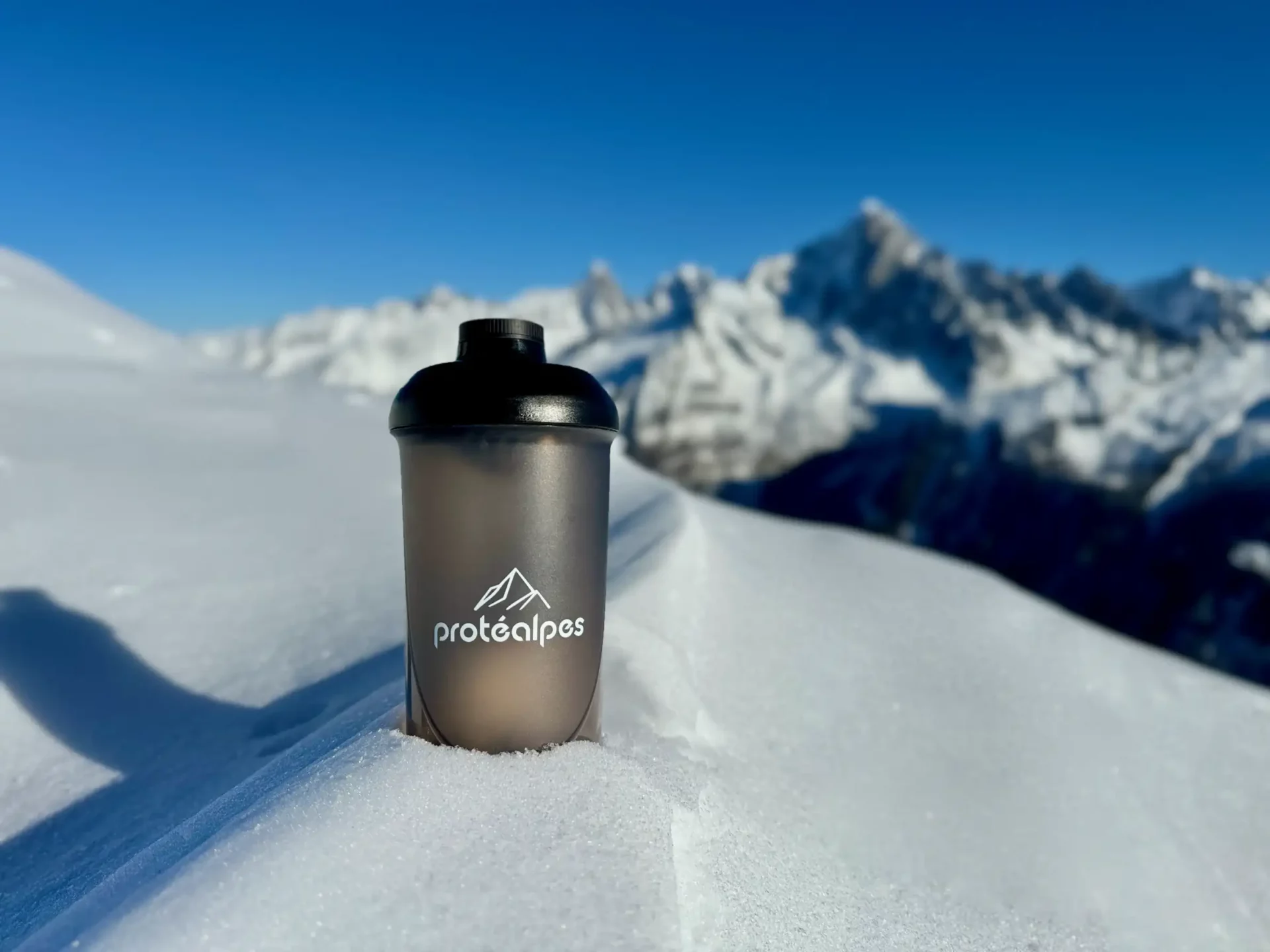 Bouteille Protéalpes sur la neige, fond de montagnes, symbolise nutrition sportive naturelle sans édulcorants ni additifs.
