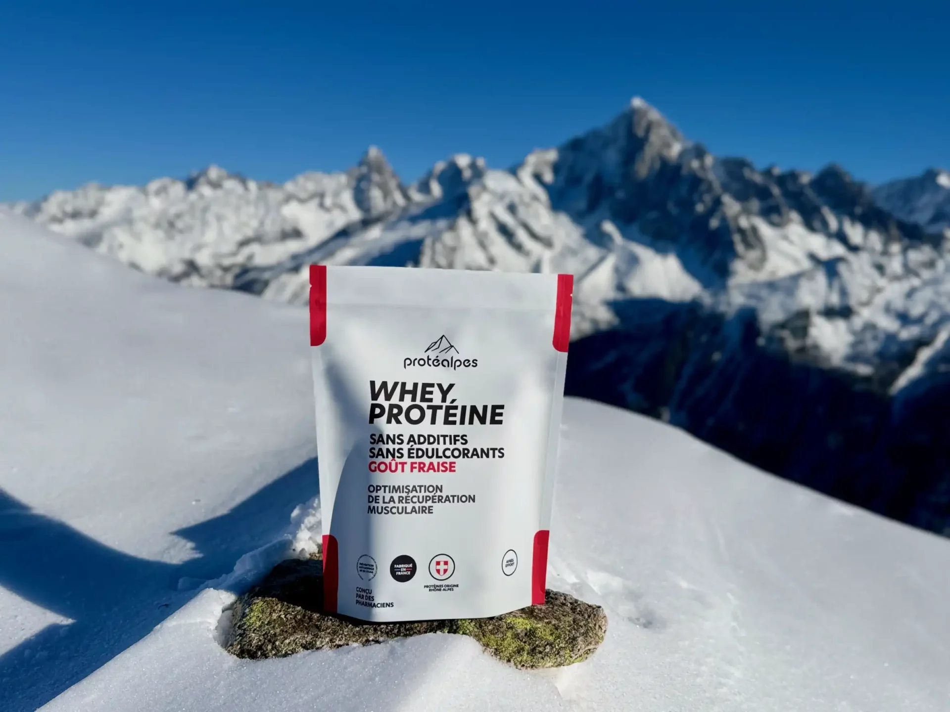 Whey Protein Pack von Protealpes ohne Zusatzstoffe oder Süßstoffe, auf Schnee platziert, Berge im Hintergrund. Erdbeergeschmack.