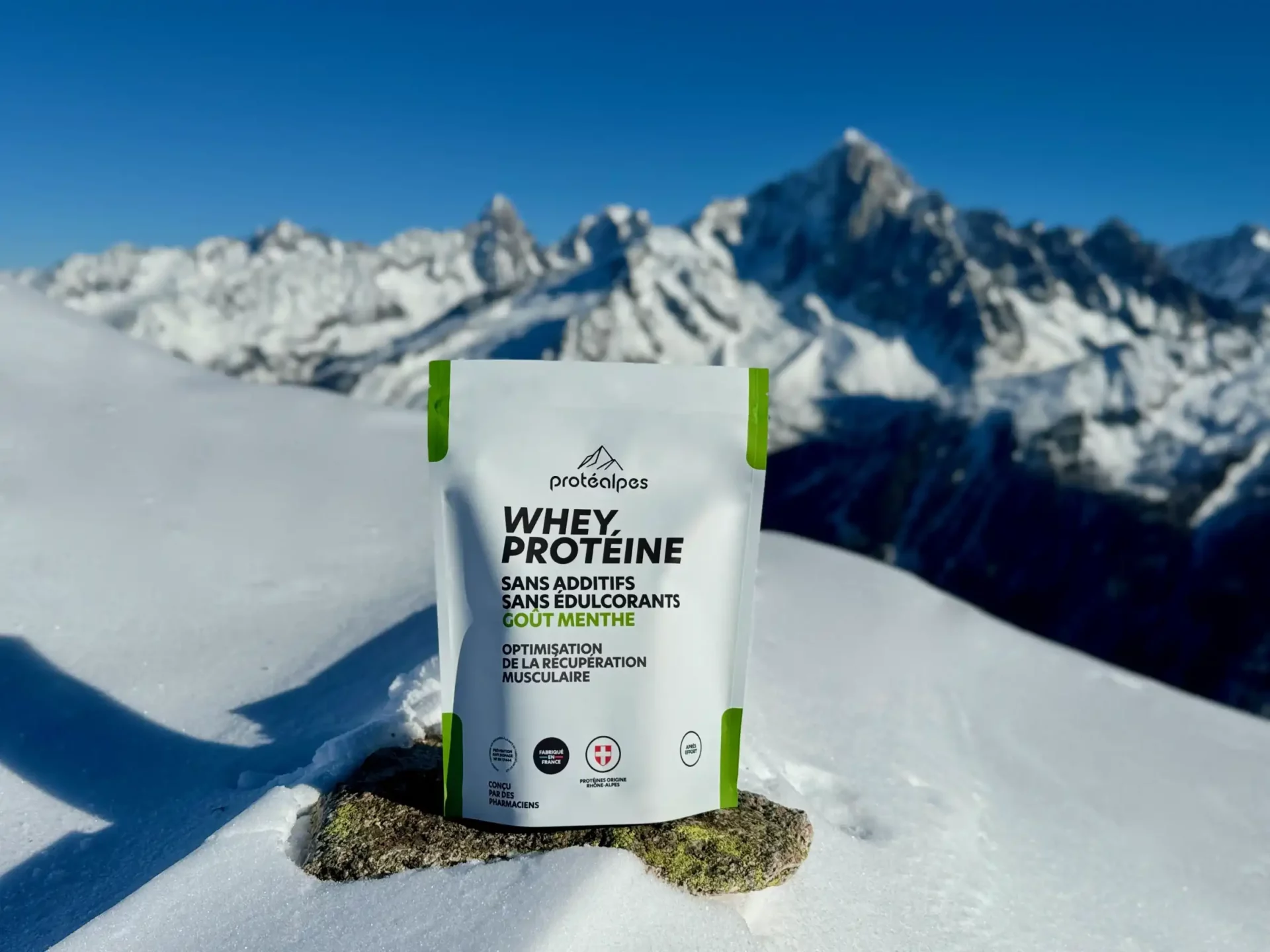 Protéalpes protein sachet on the snow, mountains in the background. No sweeteners or additives, pure sports nutrition.