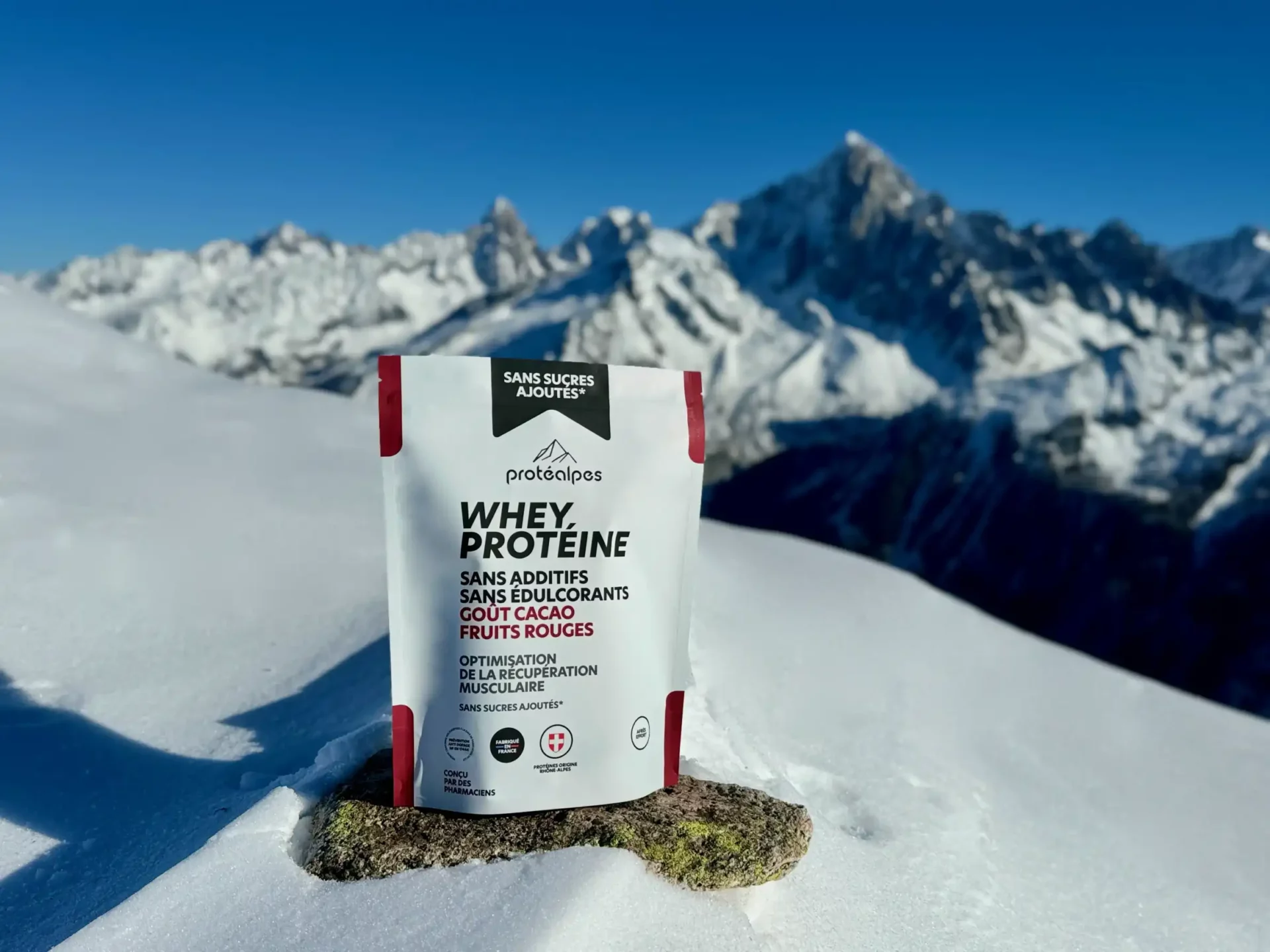 Bustina di proteine Whey Protéalpes senza additivi né edulcoranti, al gusto di cacao ai frutti rossi, con uno sfondo di montagne innevate.