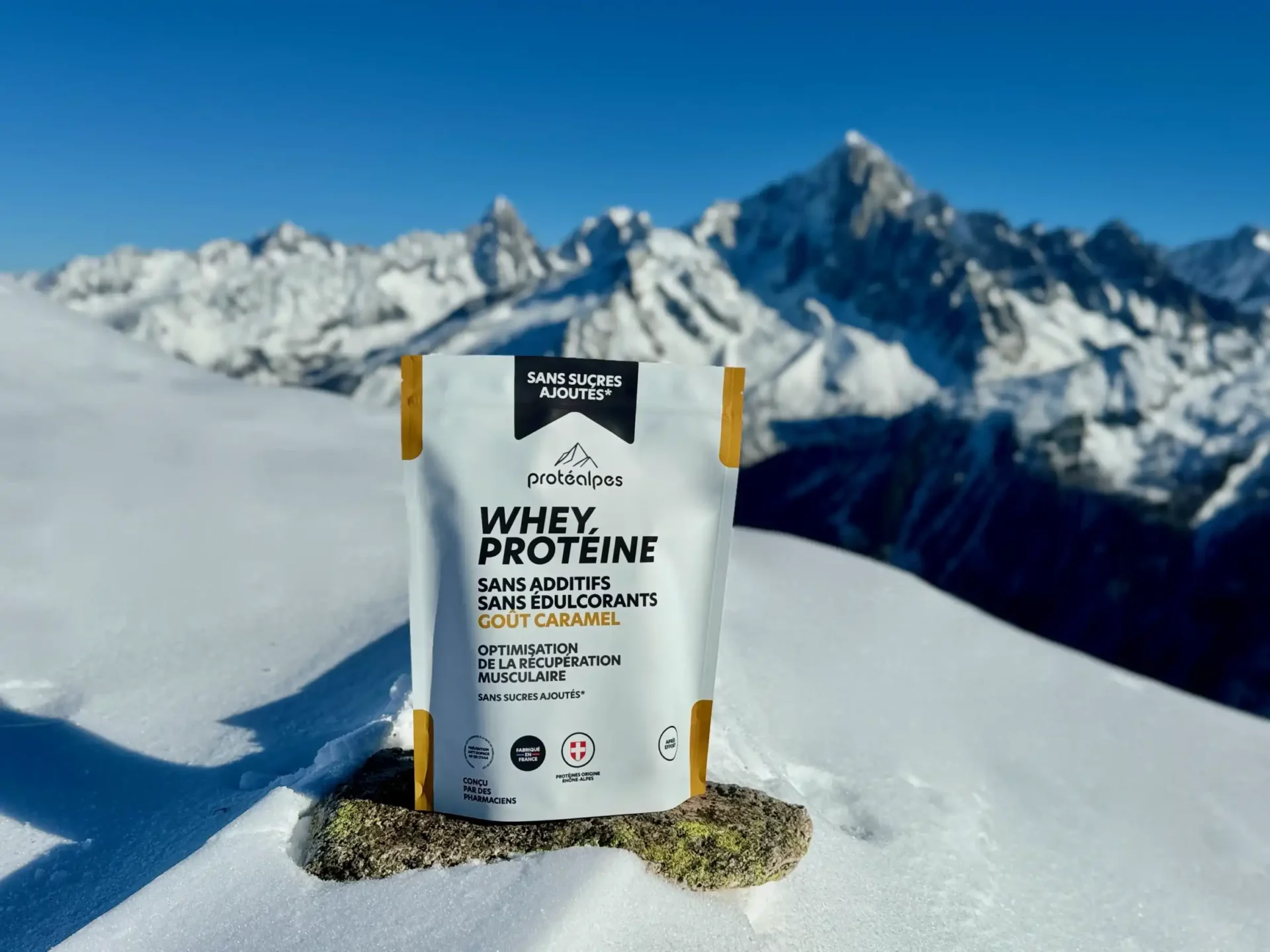 Packaging de protéine Whey Protéalpes sans additifs ni édulcorants, posé sur la neige avec un fond de montagnes enneigées.