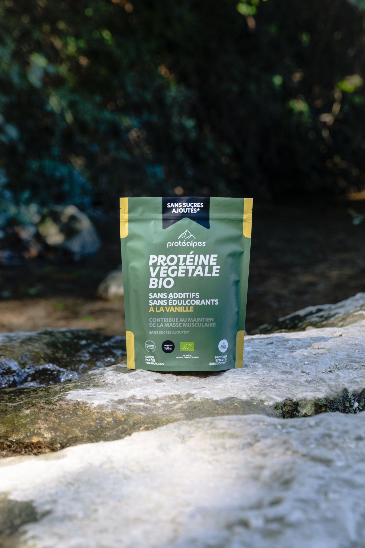 Sac de protéine végétale bio Protéalpes, sans additifs ni édulcorants, parfum vanille, au bord d'une rivière.